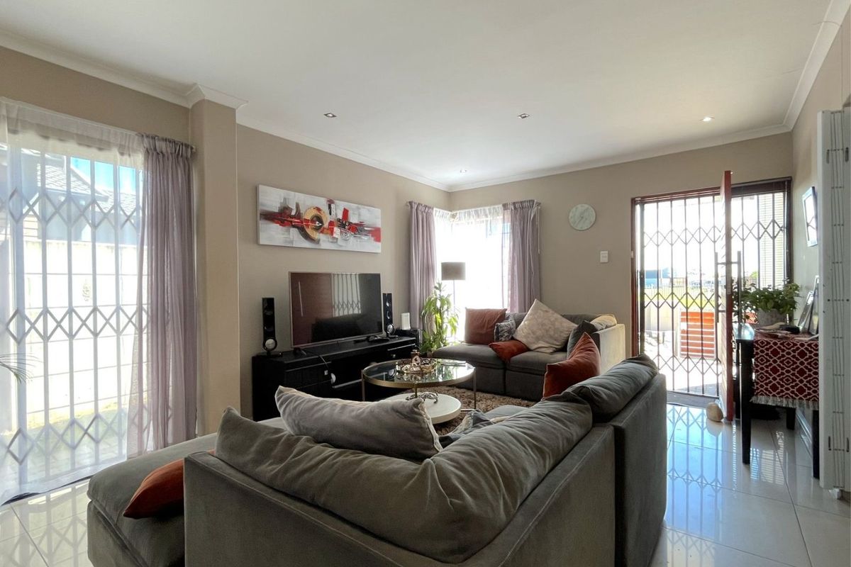 A bright and spacious living room featuring tiled flooring, recessed downlights, and direct access to the exterior through security-fitted sliding doors.