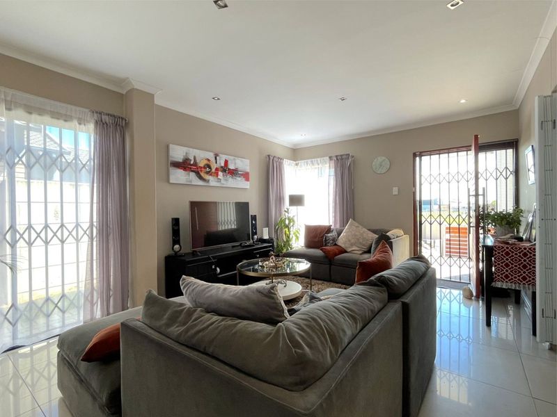 A bright and spacious living room featuring tiled flooring, recessed downlights, and direct access to the exterior through security-fitted sliding doors.