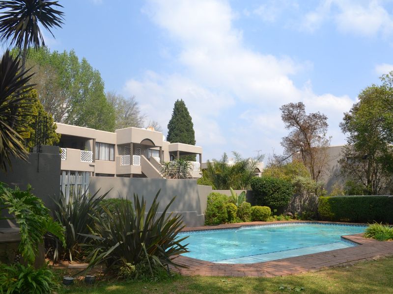 A view of the communal swimming pool area featuring brick coping, established garden landscaping, and surrounding townhouse building facades.