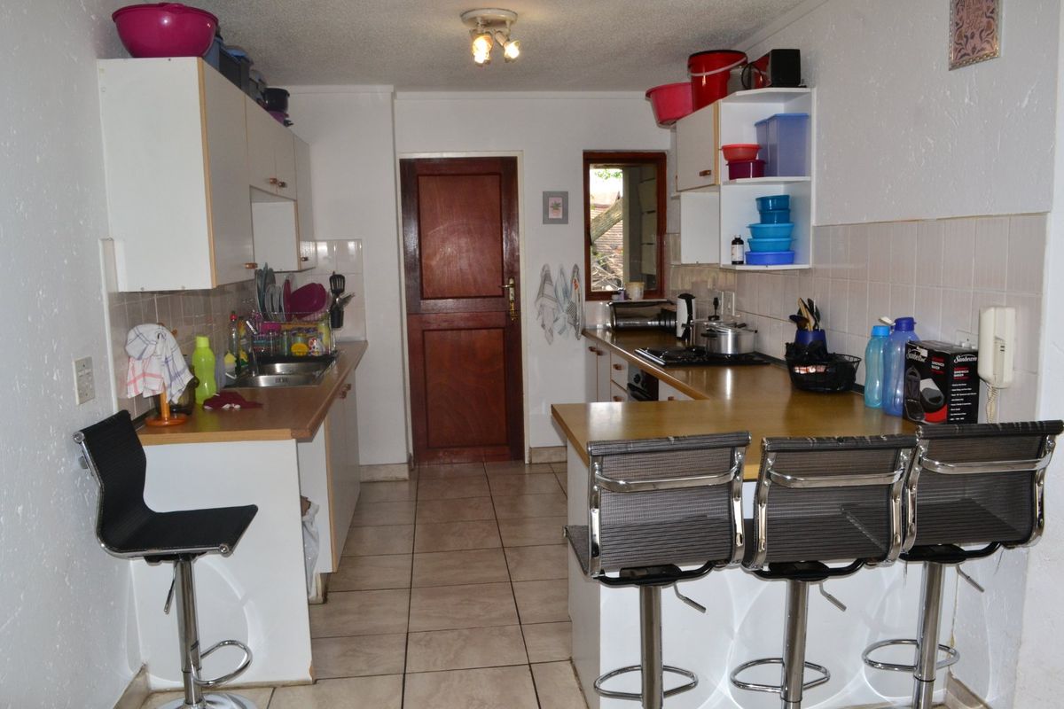 A functional kitchen featuring laminate countertops, tiled backsplash, built-in cabinetry, and a breakfast bar area with ceramic tile flooring.