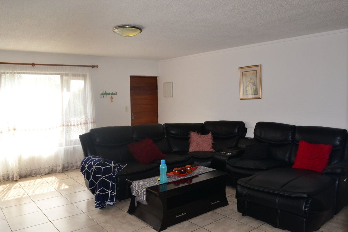 A functional living room featuring neutral tiled flooring and natural light from a large window, providing a comfortable and versatile space.