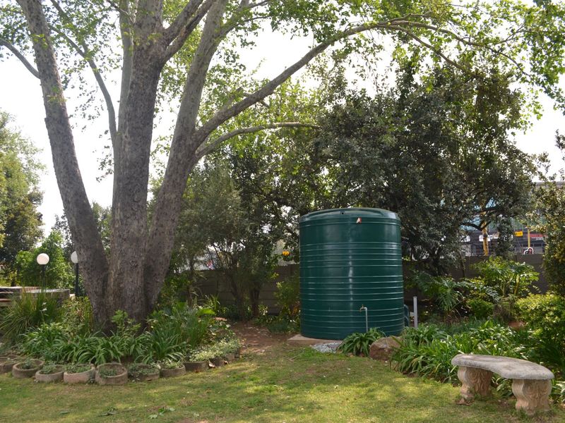 A well-maintained garden area featuring a large water storage tank, mature trees, and a built-in brick braai facility.
