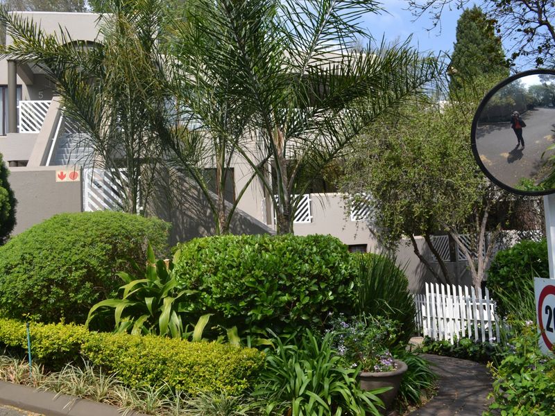 Front view of a townhouse complex featuring landscaped gardens, a paved walkway, and exterior staircases leading to upper-level balconies.