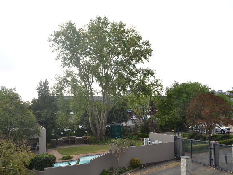 Elevated view of a rear garden featuring a swimming pool, built-in braai area, water tank, and secure boundary walling.