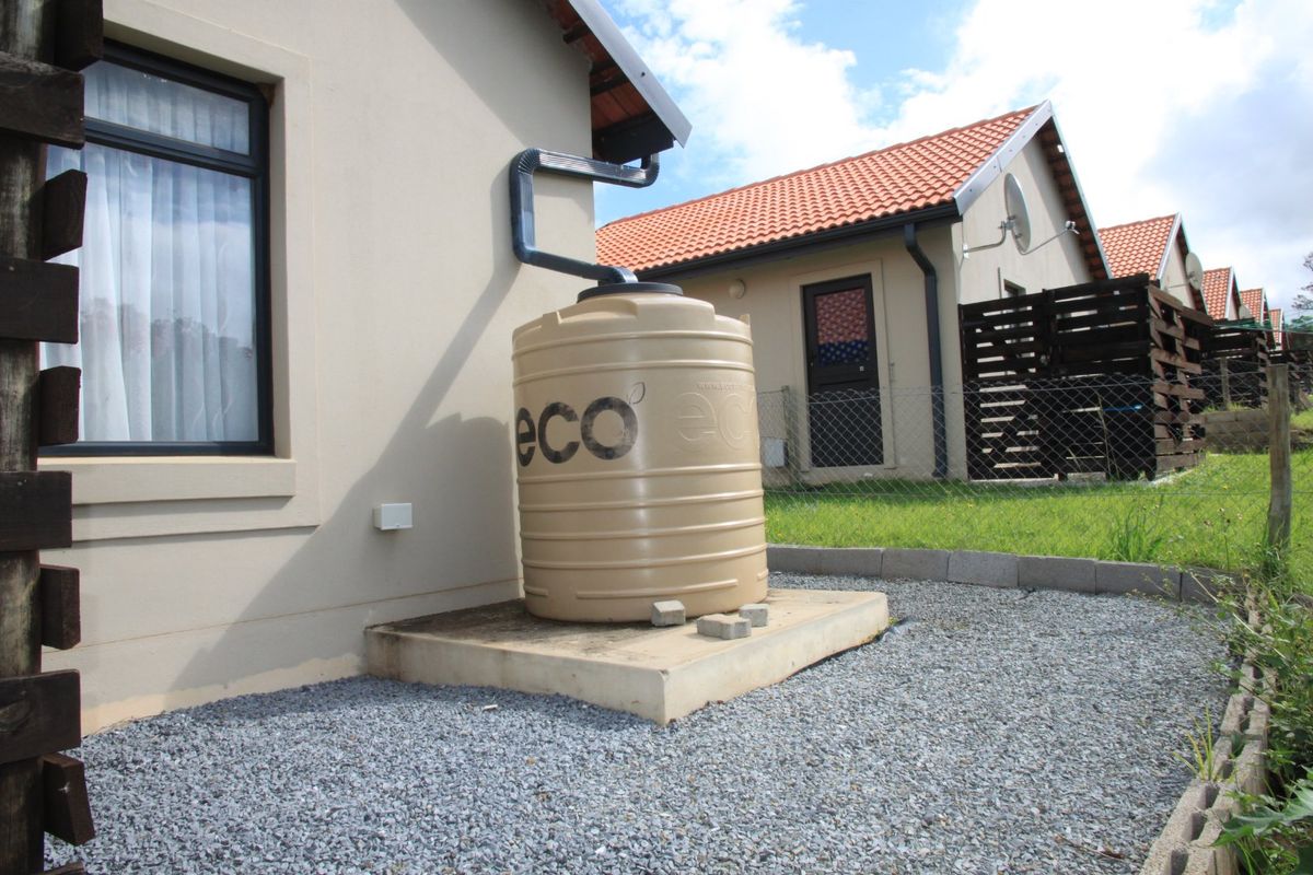Rear exterior view showing a residential property with a rainwater harvesting tank, gutter system, and gravel landscaping.
