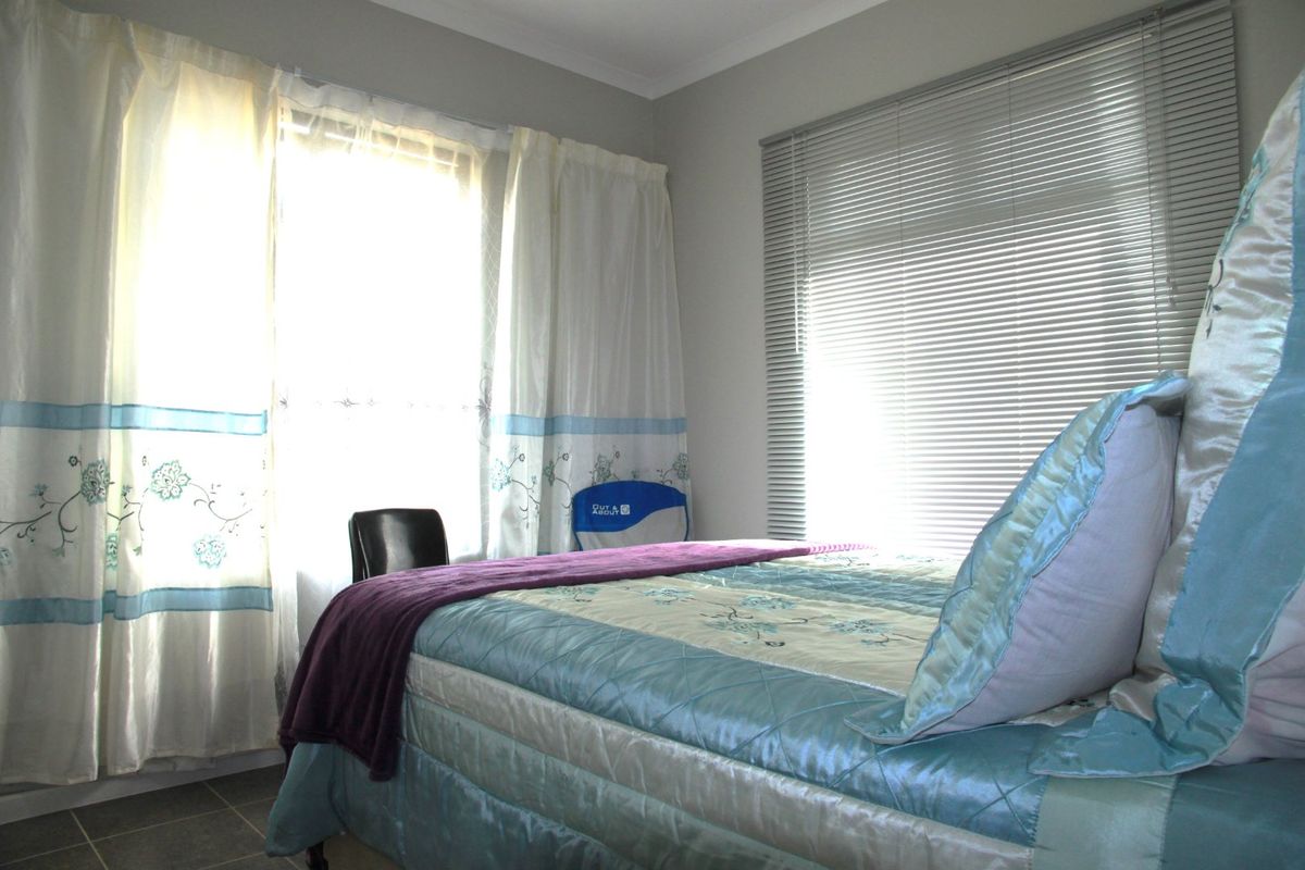 A bedroom featuring tiled flooring, window treatments including venetian blinds and curtain rails, providing natural light and a neutral wall finish.