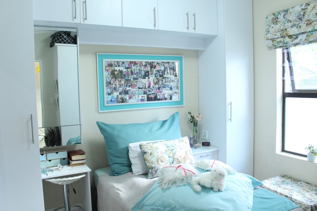 A well-maintained bedroom featuring extensive built-in cabinetry, overhead storage, and a dedicated vanity area with an integrated mirror.