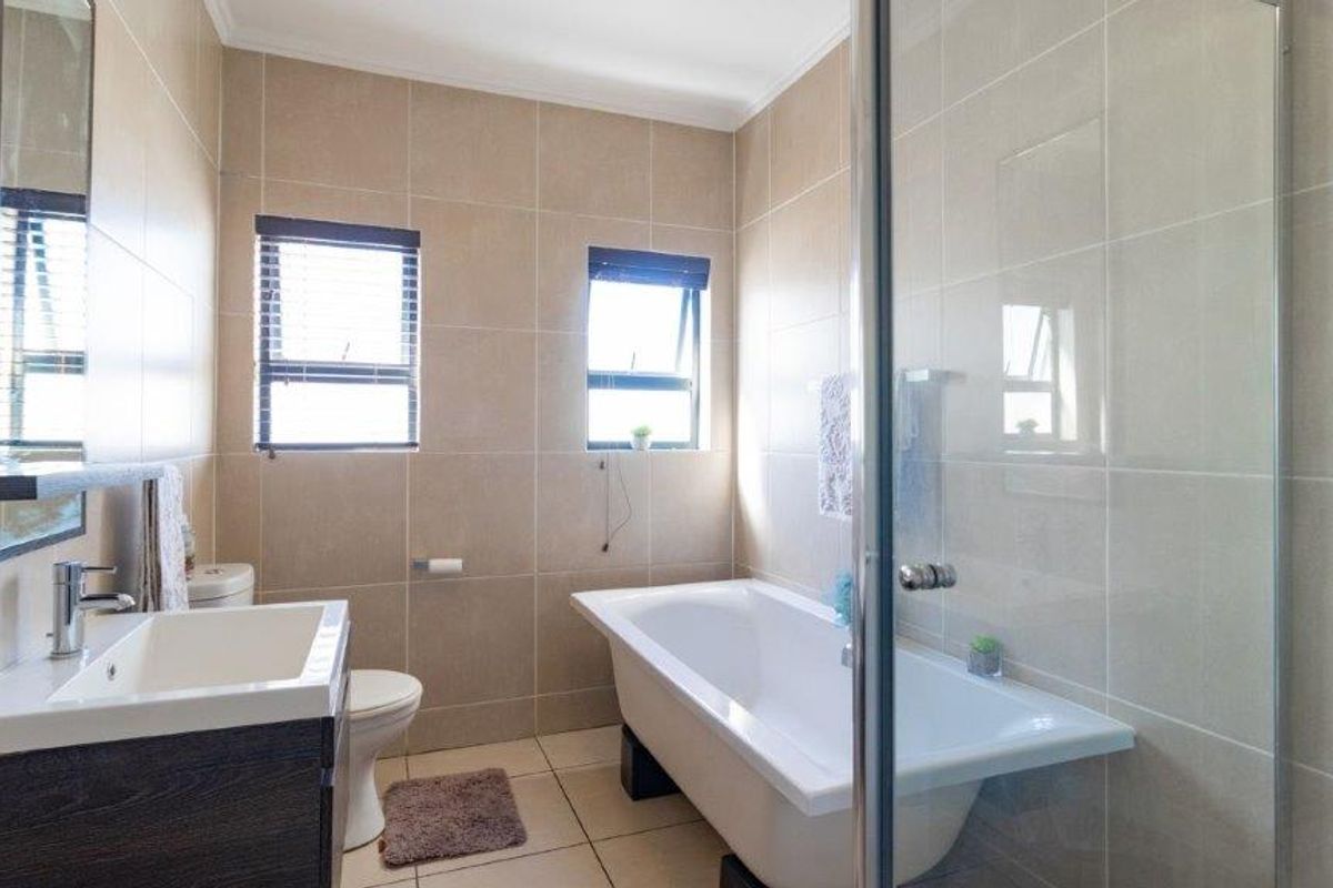 A modern bathroom featuring a freestanding bathtub, a separate glass-enclosed shower, a vanity basin, and neutral floor-to-ceiling wall tiles.
