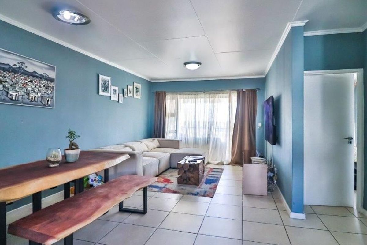 A spacious living area featuring tiled flooring, blue painted walls, and natural light through large windows.