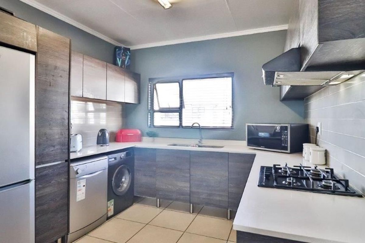 Modern kitchen featuring dark wood-grain cabinetry, stone countertops, a gas hob with extractor fan, and tiled flooring.