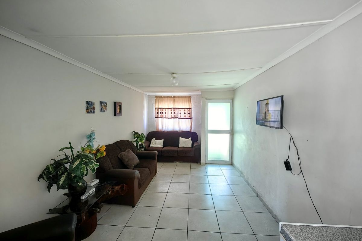 A simple living room featuring tiled flooring and a glass panel door, providing access to the exterior.
