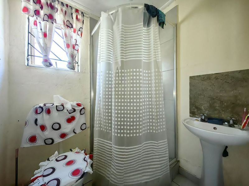 A compact bathroom featuring a shower enclosure and pedestal basin, requiring cosmetic updates and wall repairs to improve its overall condition.