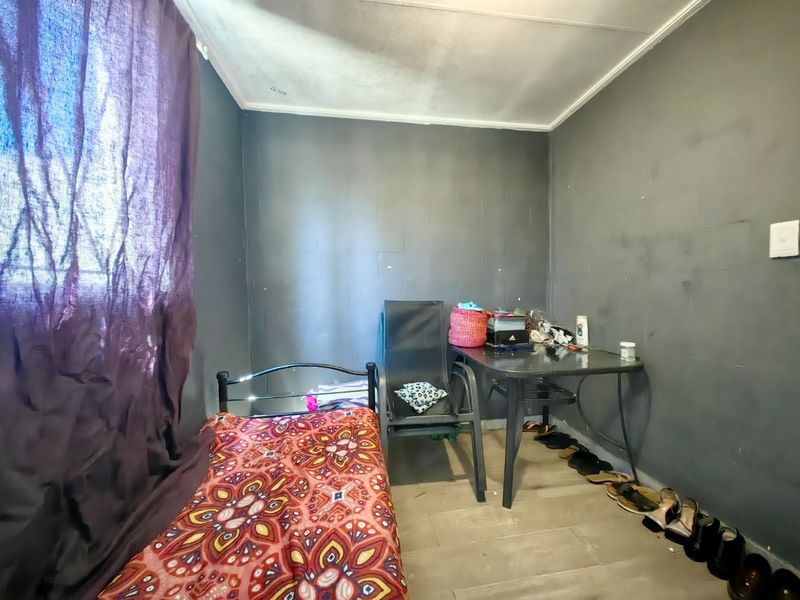 A compact bedroom featuring laminate flooring and a window with security bars, requiring cosmetic updates to the walls and ceiling.