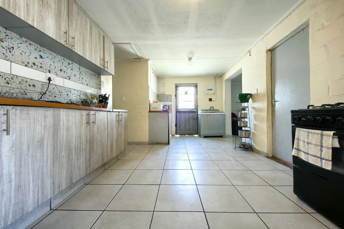 A functional kitchen featuring wood-look cabinetry, terrazzo-style backsplash, tiled flooring, and a rear exit with a security gate.