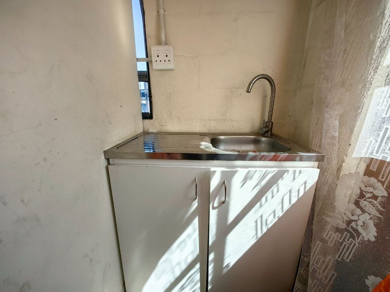 A compact scullery or utility area featuring a stainless steel sink, gooseneck faucet, and built-in cabinetry, requiring cosmetic updates to the wall finishes.