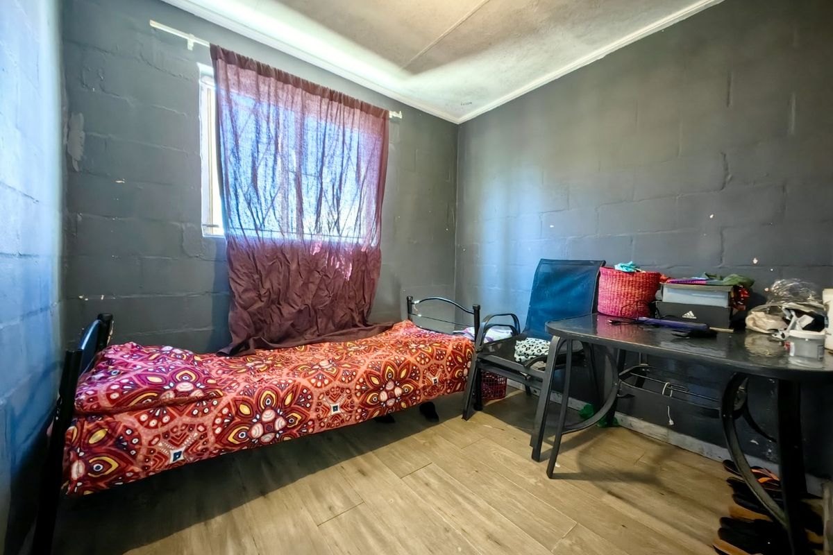 A compact bedroom featuring tiled flooring and painted blockwork walls, providing a functional space with basic finishes.