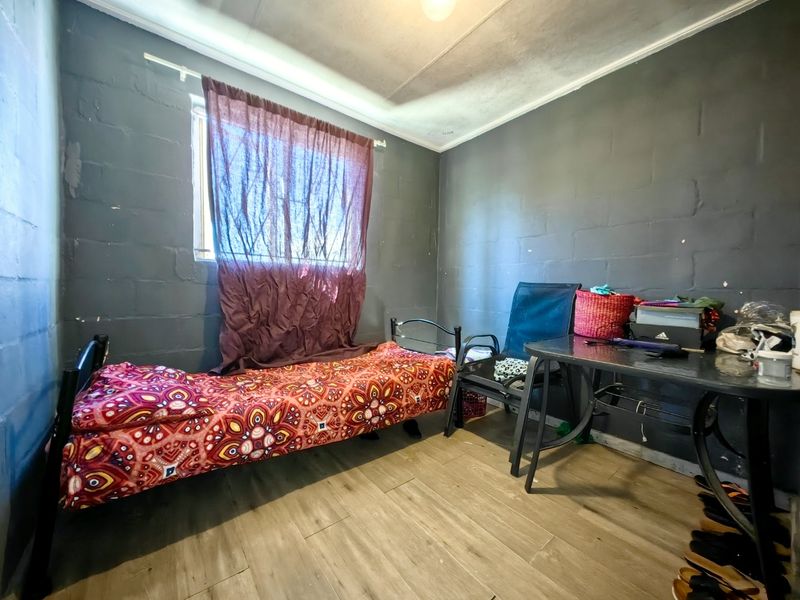 A compact bedroom featuring tiled flooring and painted blockwork walls, providing a functional space with basic finishes.