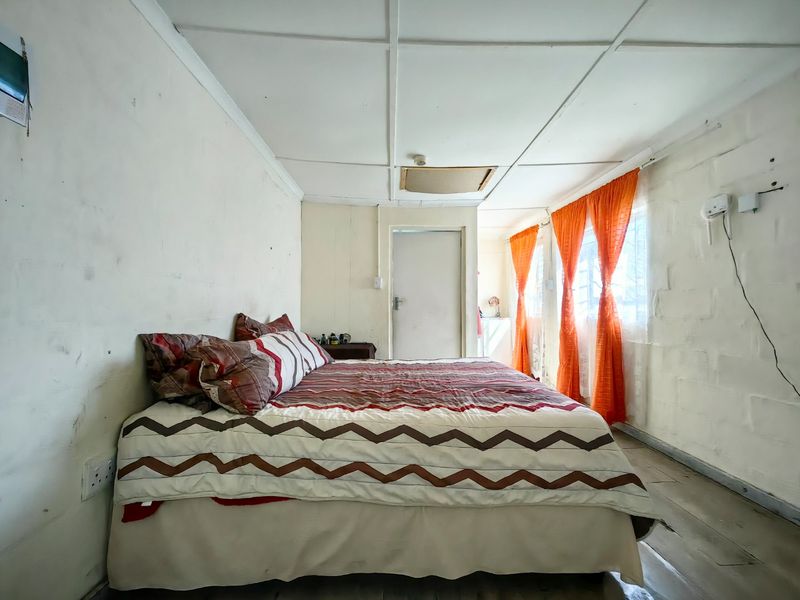 A bedroom featuring exposed blockwork walls and a panelled ceiling, offering a basic layout with potential for cosmetic updates.