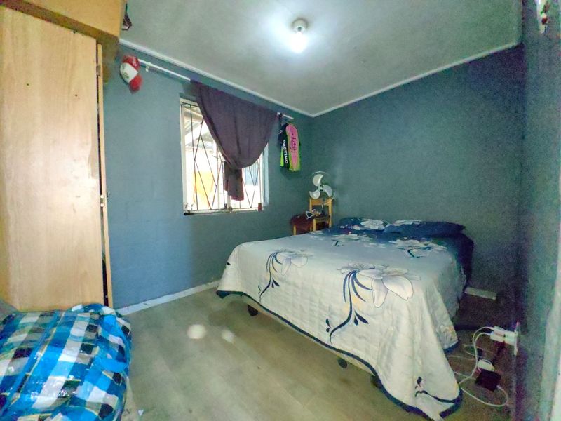 A compact bedroom featuring laminate flooring, a built-in wardrobe, and a window fitted with security bars.