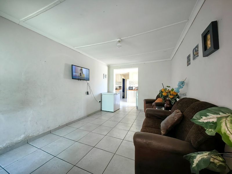 A living room area featuring tiled flooring and neutral wall finishes, providing a functional space with direct access to the kitchen area.