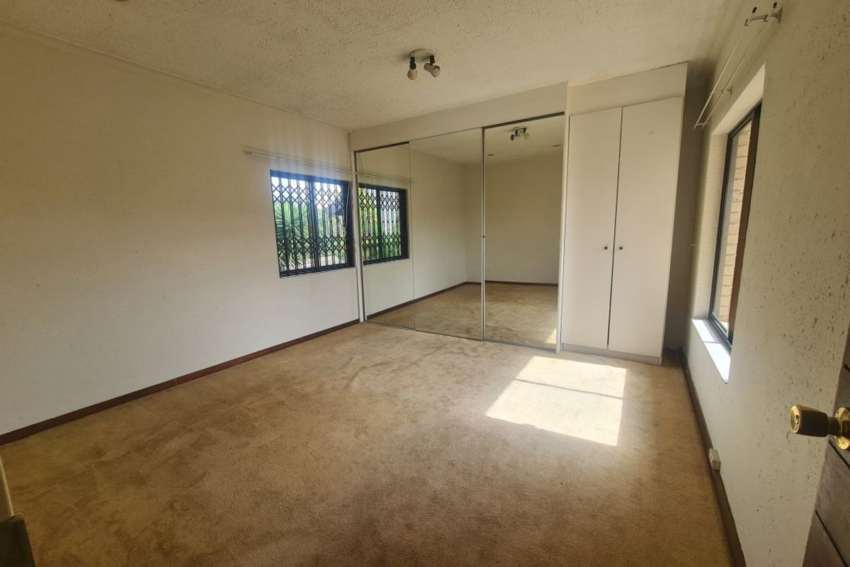 Empty bedroom featuring built-in mirrored wardrobes, additional cupboard storage, and security bars on the windows.