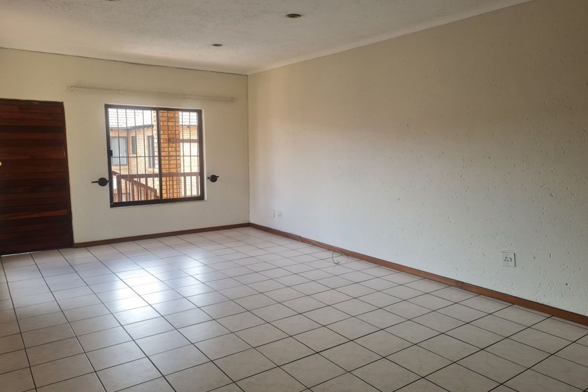 An empty, open-plan living area featuring neutral tiled flooring, recessed lighting, and a window with security bars, offering a blank canvas for interior design.