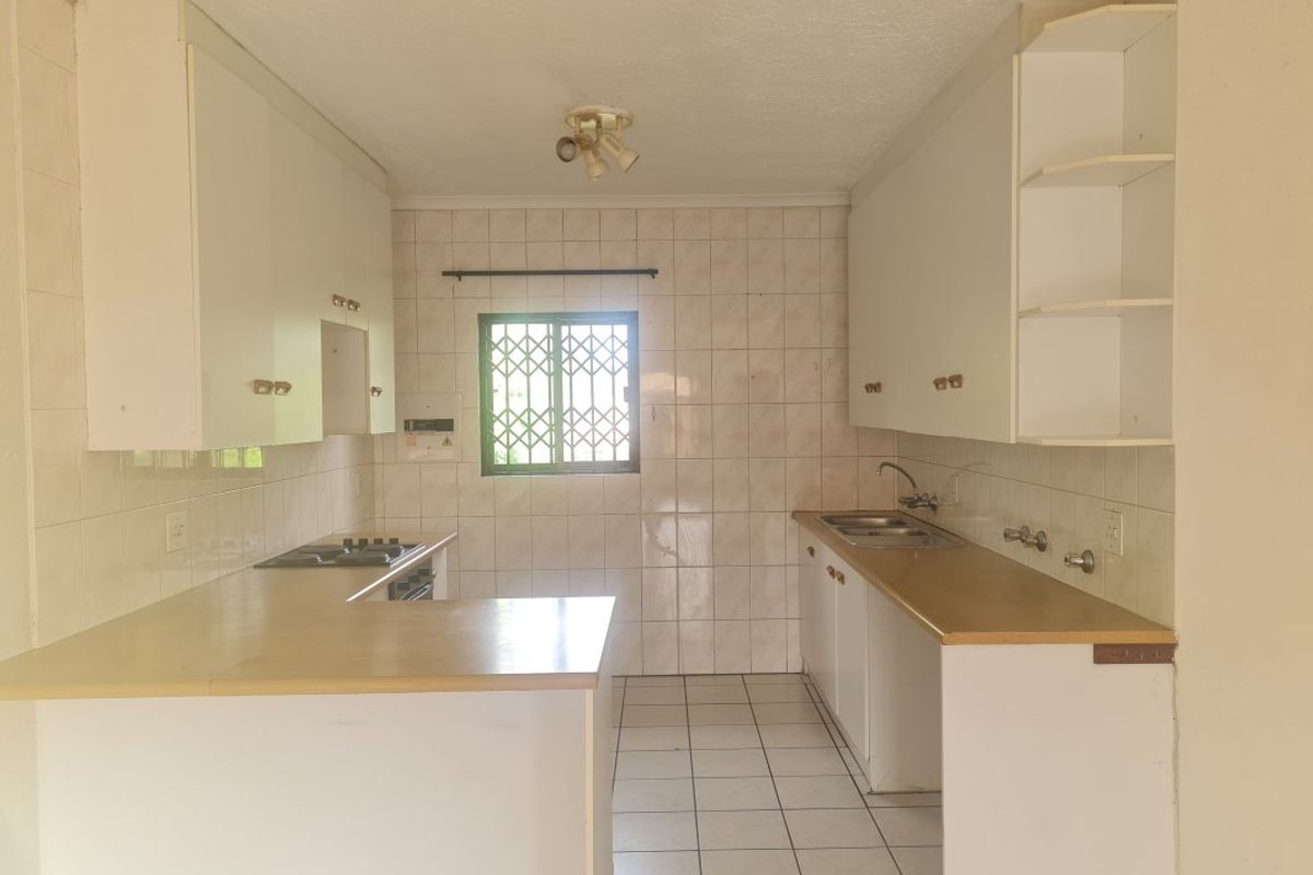 A functional kitchen featuring built-in cabinetry, laminate countertops, a double bowl sink, and a built-in hob, finished with ceramic wall and floor tiles.