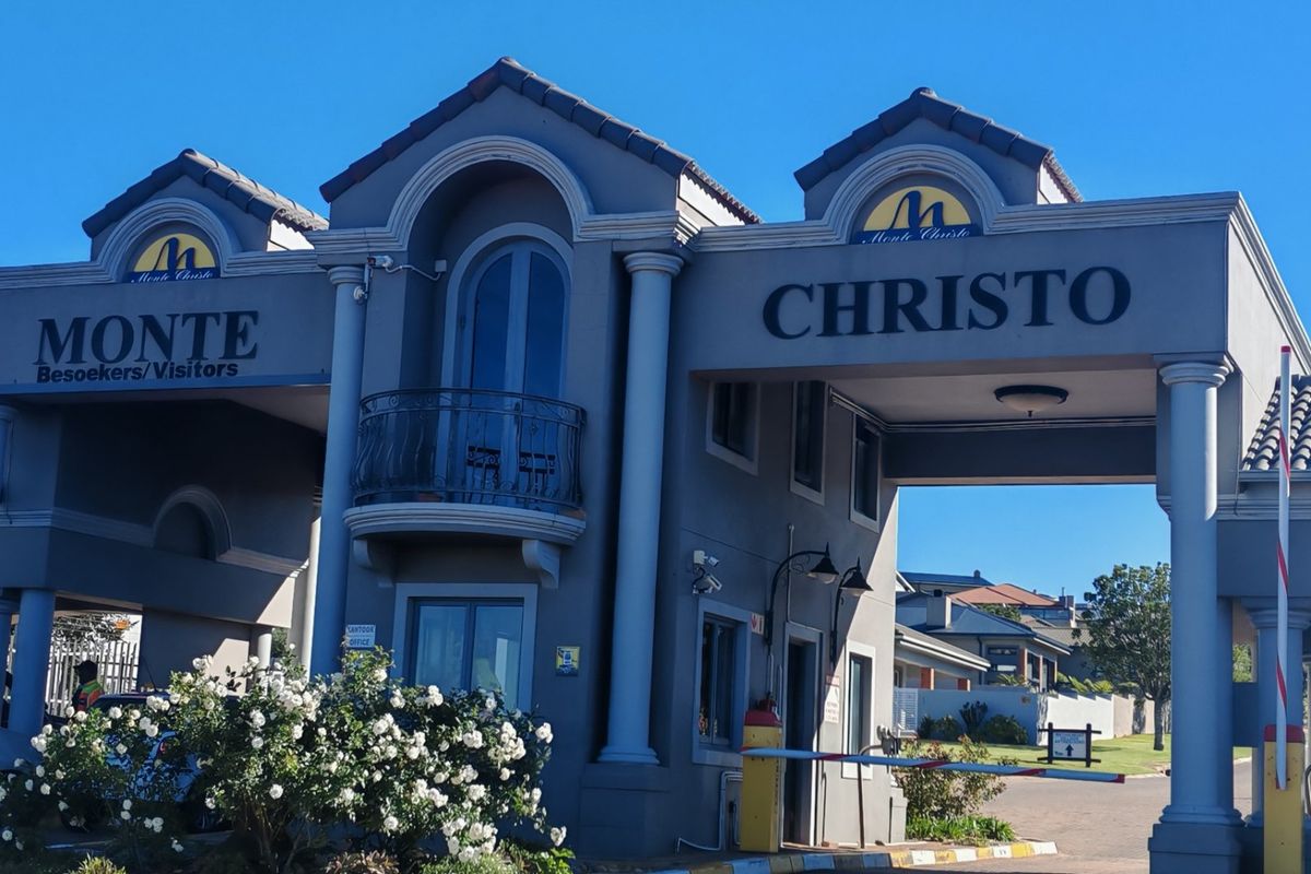 The main entrance gatehouse of Monte Christo estate, featuring a secure boom gate, architectural columns, and a balcony.