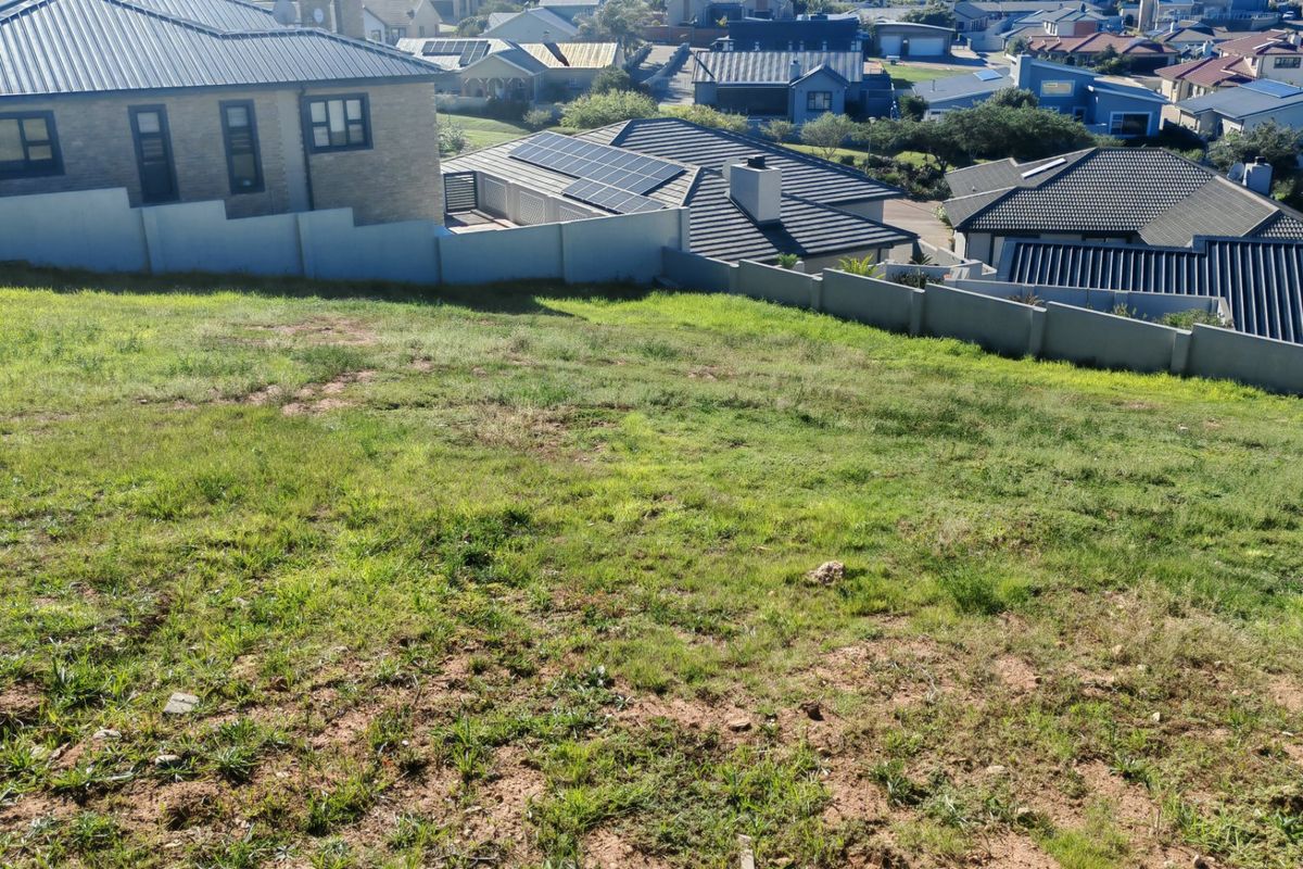 An elevated view of a vacant residential plot featuring a gentle slope and established boundary walls in a developed neighborhood.