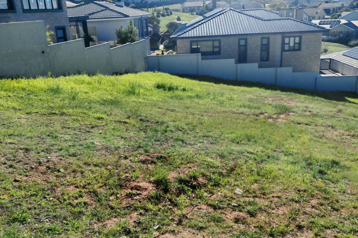 A sloped vacant residential plot enclosed by boundary walls, situated within a developed suburban estate.