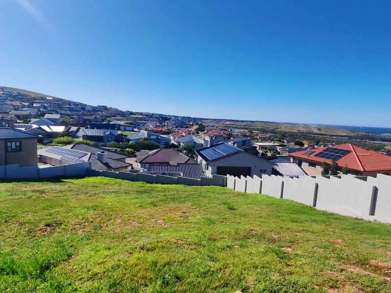 Elevated view overlooking a residential estate with coastal landscape in the distance, featuring a sloping grass plot with concrete boundary walls.