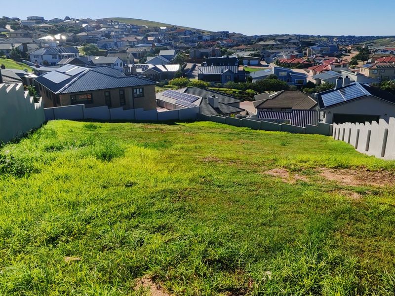 A view from a vacant residential plot overlooking a developed suburban neighborhood with established housing.