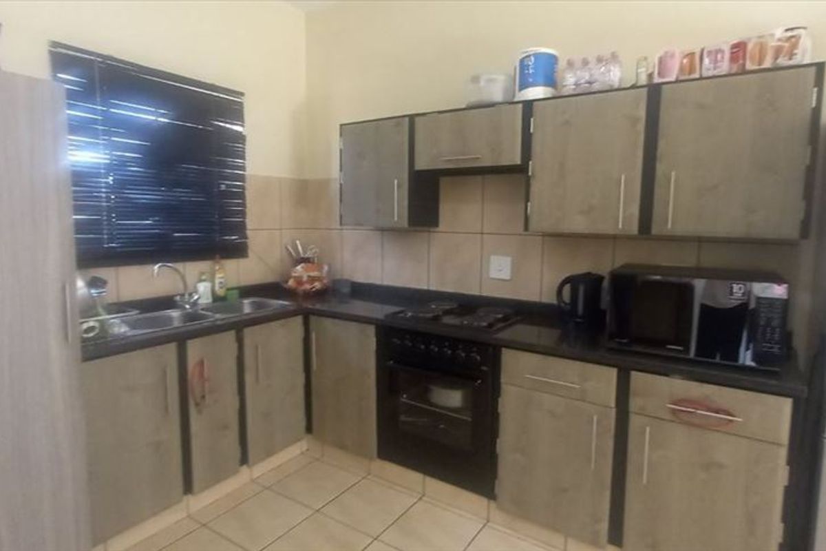 A functional kitchen featuring built-in cabinetry, black granite countertops, a double sink, and integrated oven and hob with tiled splashbacks and flooring.