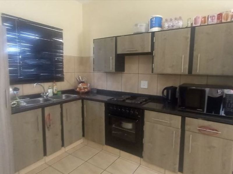 A functional kitchen featuring built-in cabinetry, black granite countertops, a double sink, and integrated oven and hob with tiled splashbacks and flooring.