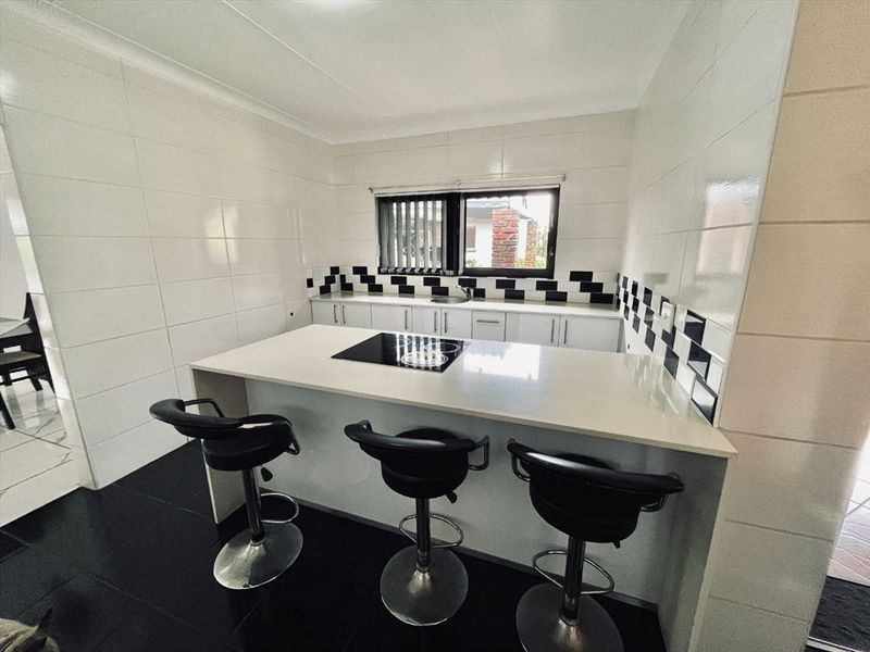 A functional kitchen featuring a central island with a built-in cooktop, contrasting black and white tiled splashback, and ample under-counter storage.