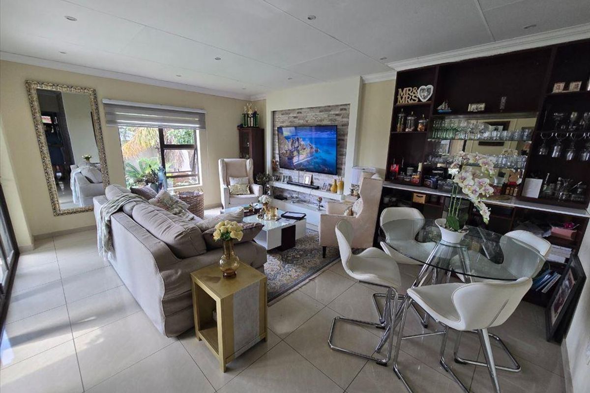 Spacious open-plan living area featuring tiled flooring, a built-in stone-cladding media wall, and a custom integrated bar unit with shelving.