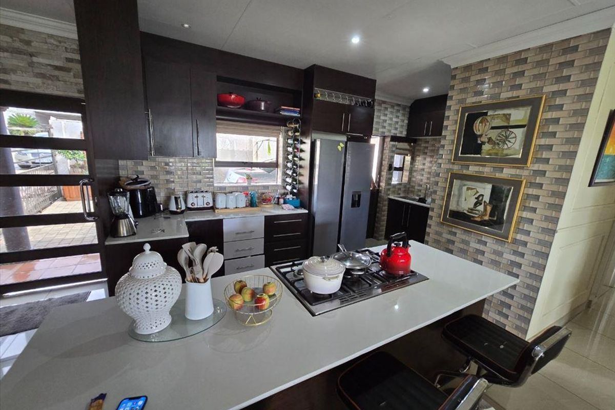 Modern kitchen featuring dark cabinetry, stone countertops, a central island with a built-in gas hob, and decorative brick-style feature wall tiling.