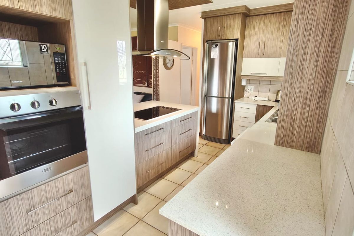 Modern kitchen featuring wood-grain cabinetry, stone countertops, built-in oven, microwave, and hob with a stainless steel extractor fan.