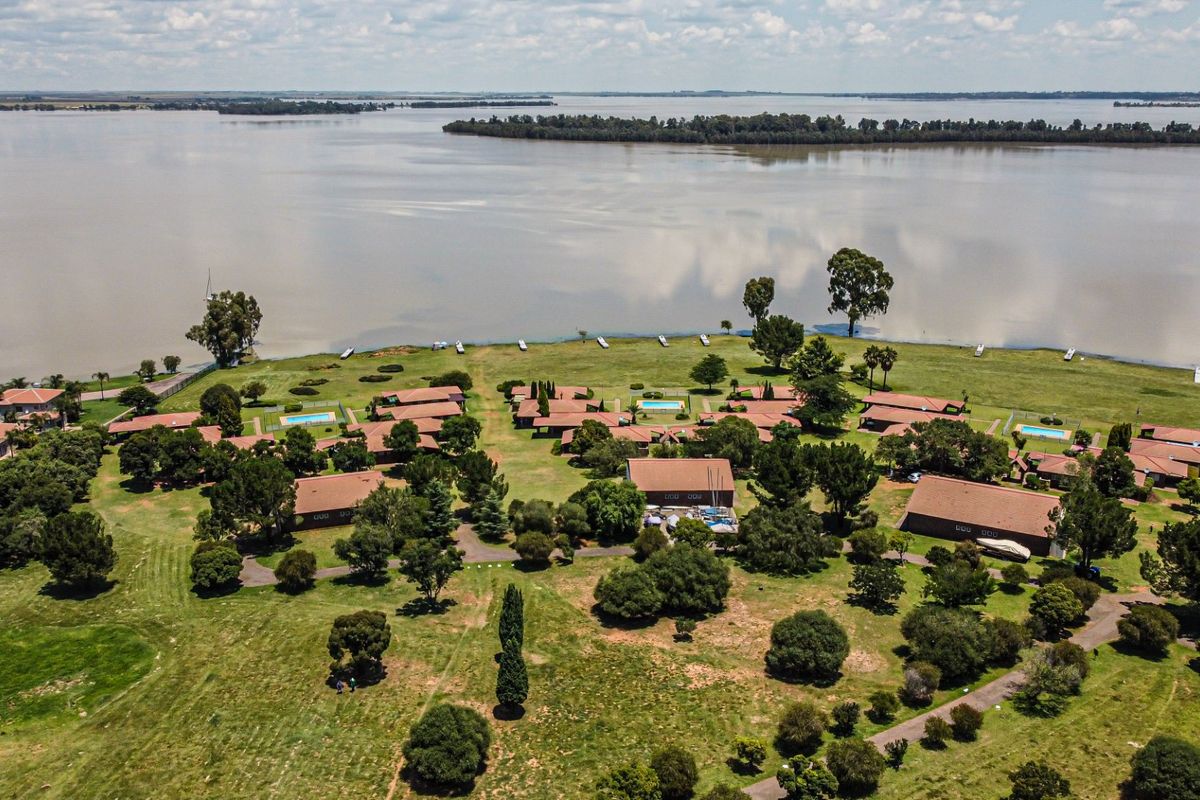 Aerial view of a residential estate featuring multiple dwellings, swimming pools, and expansive landscaped grounds situated along a large waterfront.