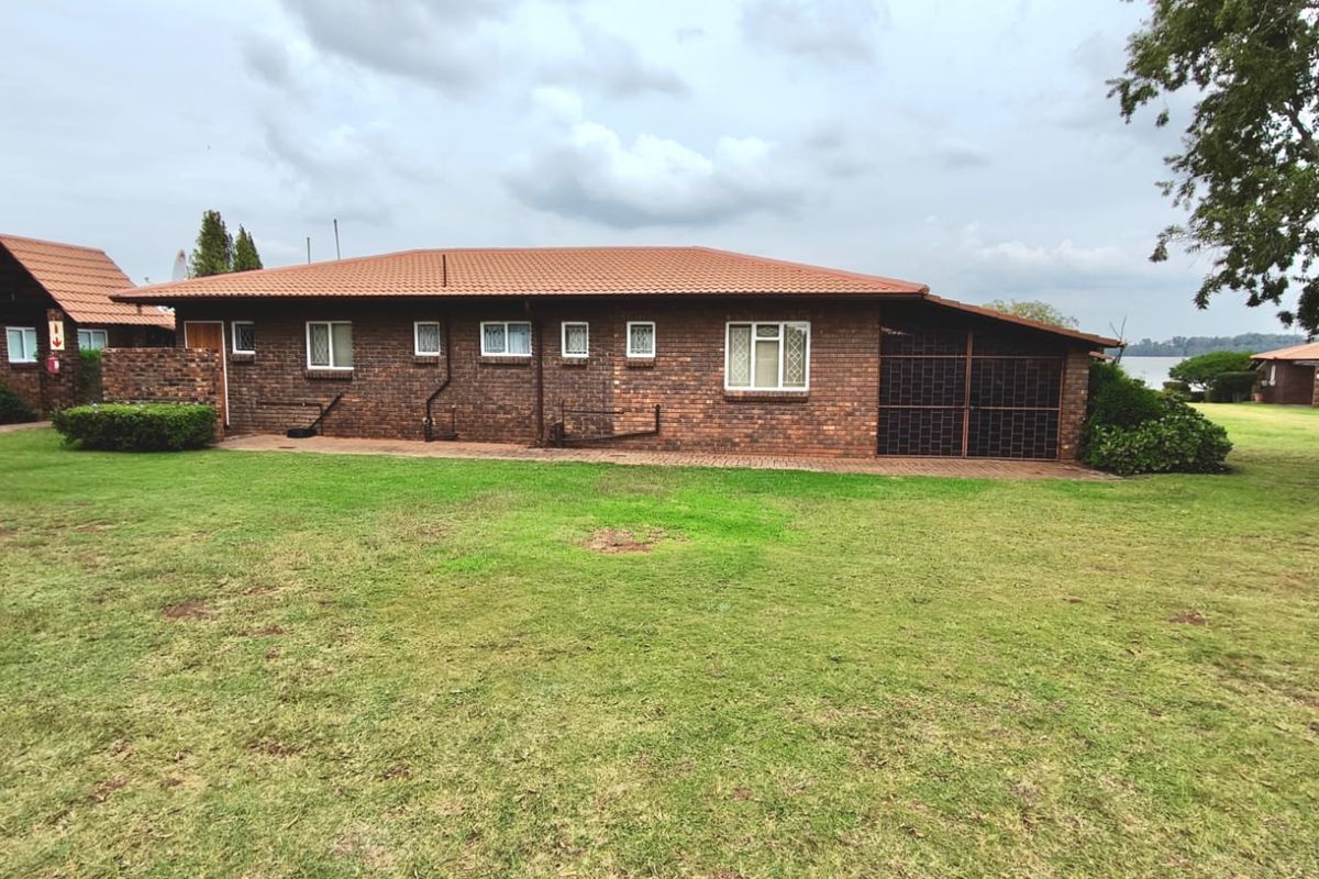 A view of the rear exterior of a face brick house featuring a tiled roof, security gate, and surrounding lawn area.