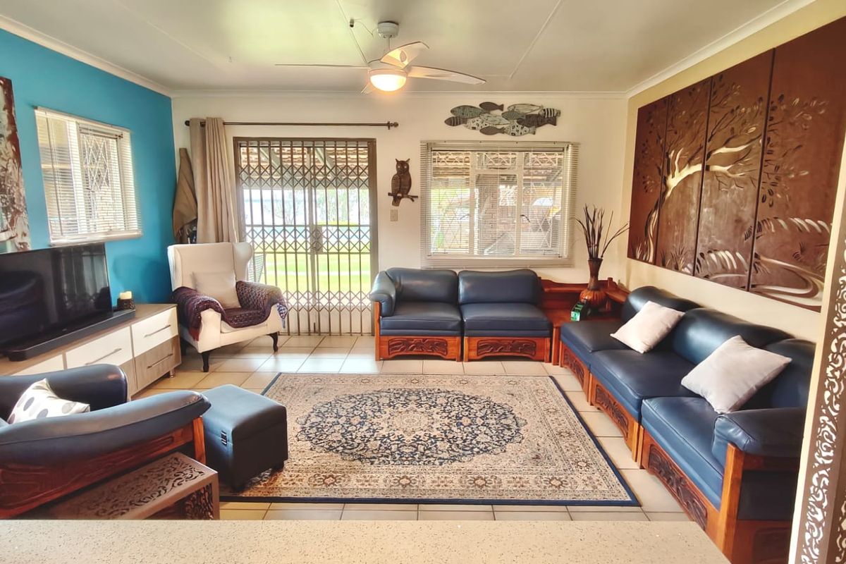 A spacious living room featuring tiled flooring, a ceiling fan, and a sliding door with a security gate leading to the exterior.