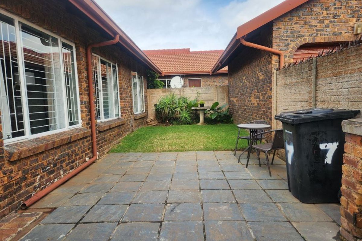 A private rear courtyard featuring a paved patio area, brick townhouse exterior, and a small lawn section enclosed by boundary walls.
