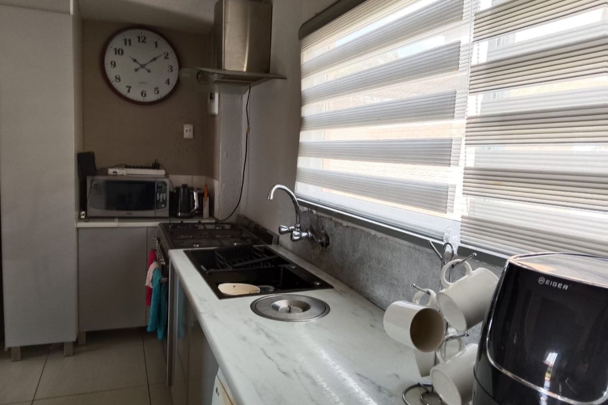 A functional kitchen featuring a gas hob, stainless steel extractor fan, marble-look countertops, and an undermount sink with modern roller blinds.