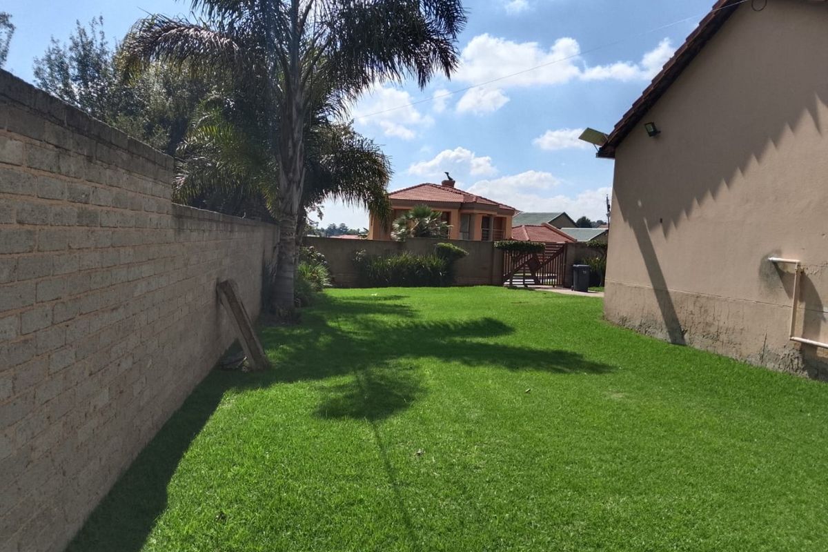 A private rear garden featuring a well-maintained lawn, enclosed by a brick boundary wall with exterior lighting fixtures.