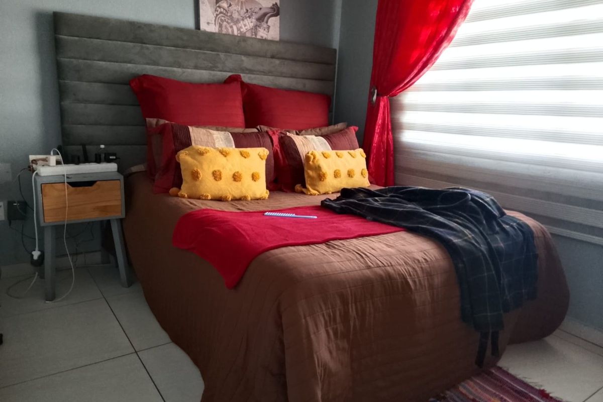 A bedroom featuring a large upholstered headboard, tiled flooring, and modern roller blinds, providing a functional and comfortable sleeping space.