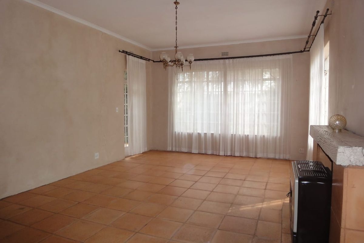 Spacious living room featuring terracotta tiled flooring, a central chandelier, and a built-in fireplace, offering a blank canvas for renovation.