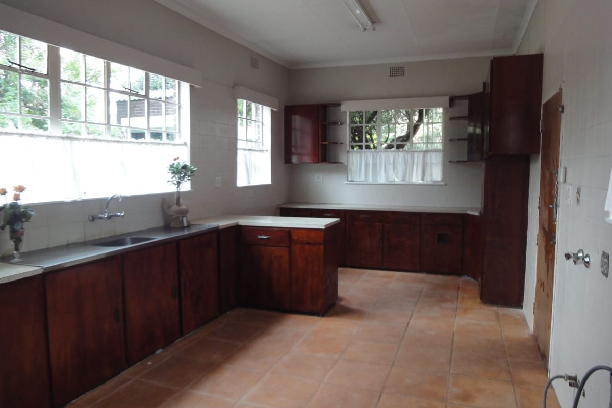 A spacious, dated kitchen featuring original wooden cabinetry, tiled flooring, and large windows providing ample natural light, ready for a modern renovation.