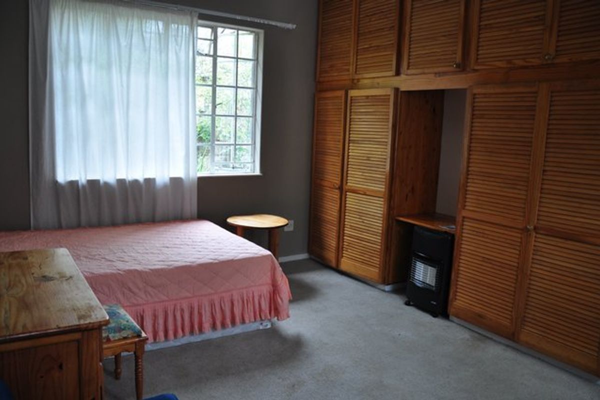 A bedroom featuring extensive floor-to-ceiling built-in wooden cupboards with louvered doors and a window providing natural light.