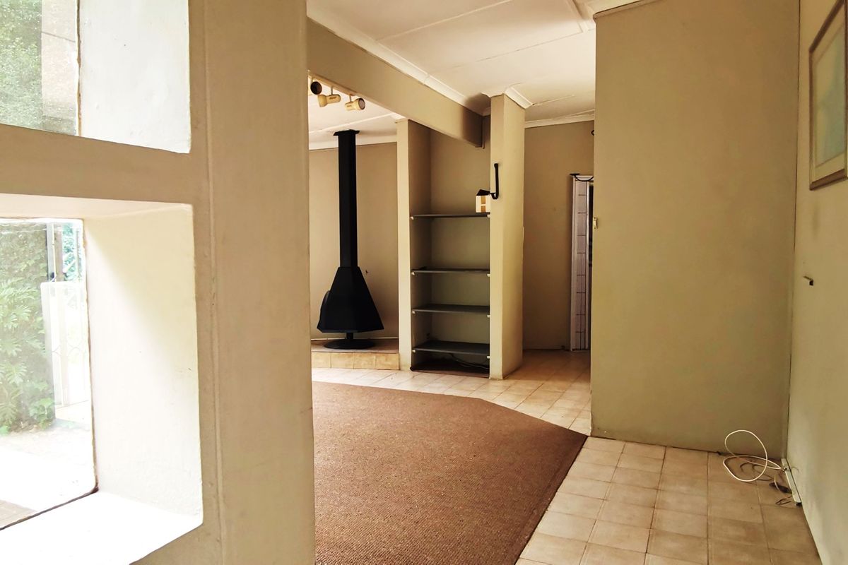 Spacious living area featuring a central freestanding fireplace, built-in shelving, and a combination of tiled and carpeted flooring with natural light.