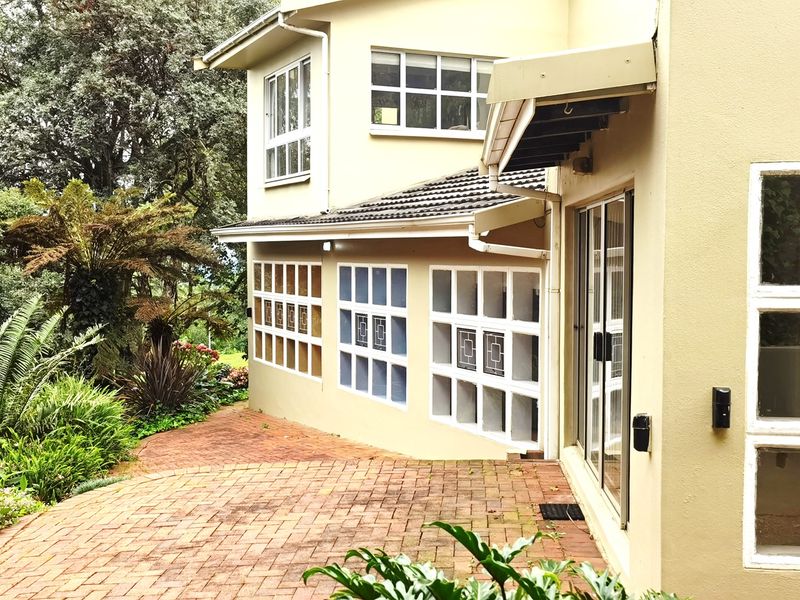 Rear exterior view of the house featuring a brick paved patio area, sliding glass doors, and established garden surroundings.
